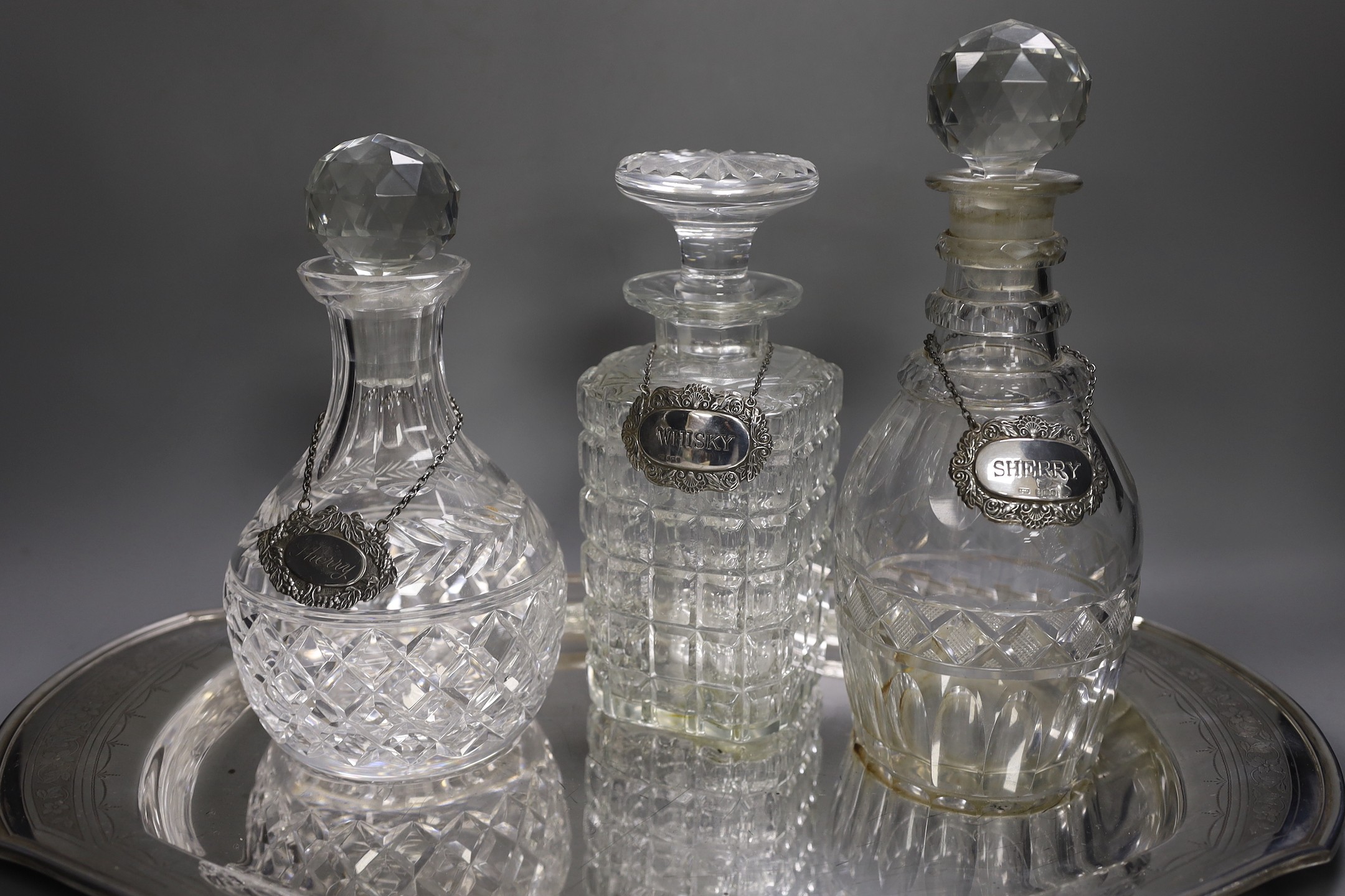 A silver plated oval tray, five assorted cut glass decanters and five assorted silver wine labels.